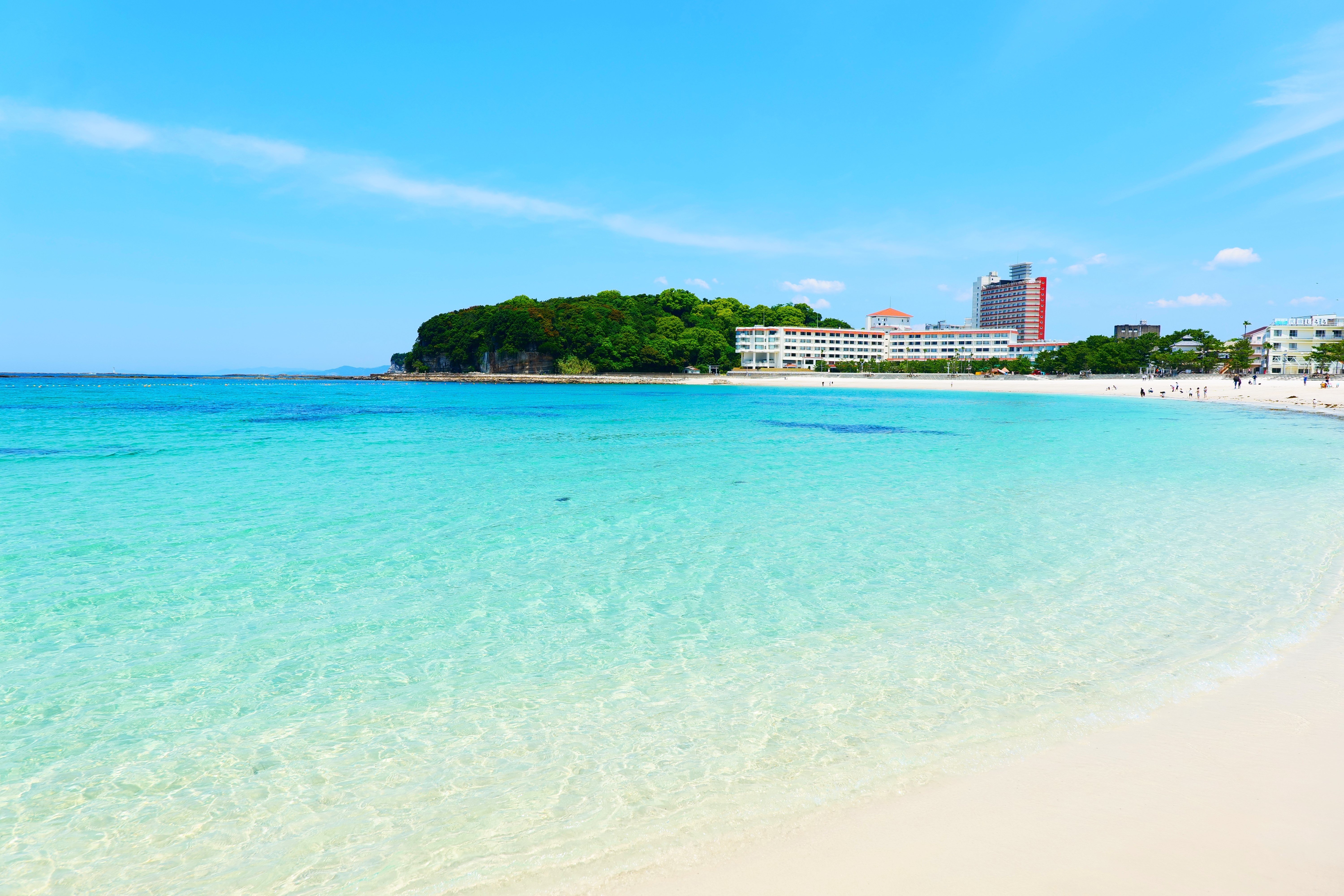 Shirahama Beach in Wakayama, Japan, with clear turquoise water, white sand, seaside hotels, and a green coastline under a bright blue sky.