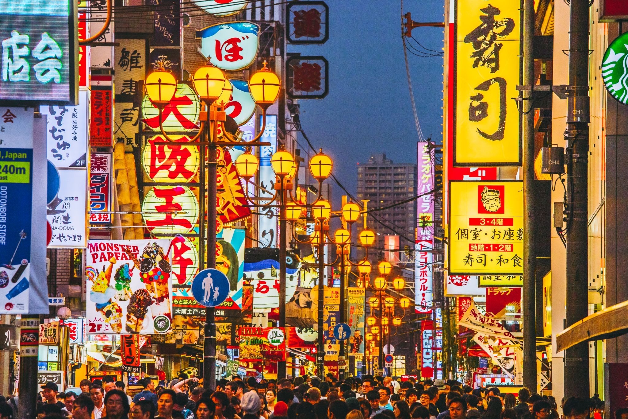 Visitors walking through Dotonbori in Osaka, surrounded by bright restaurant signs and nightlife.