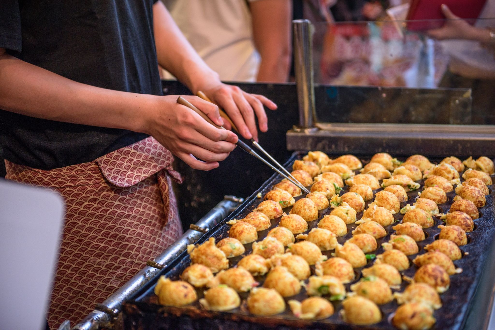 Takoyaki vendor cooking rows of Osaka-style octopus balls on a hot griddle.