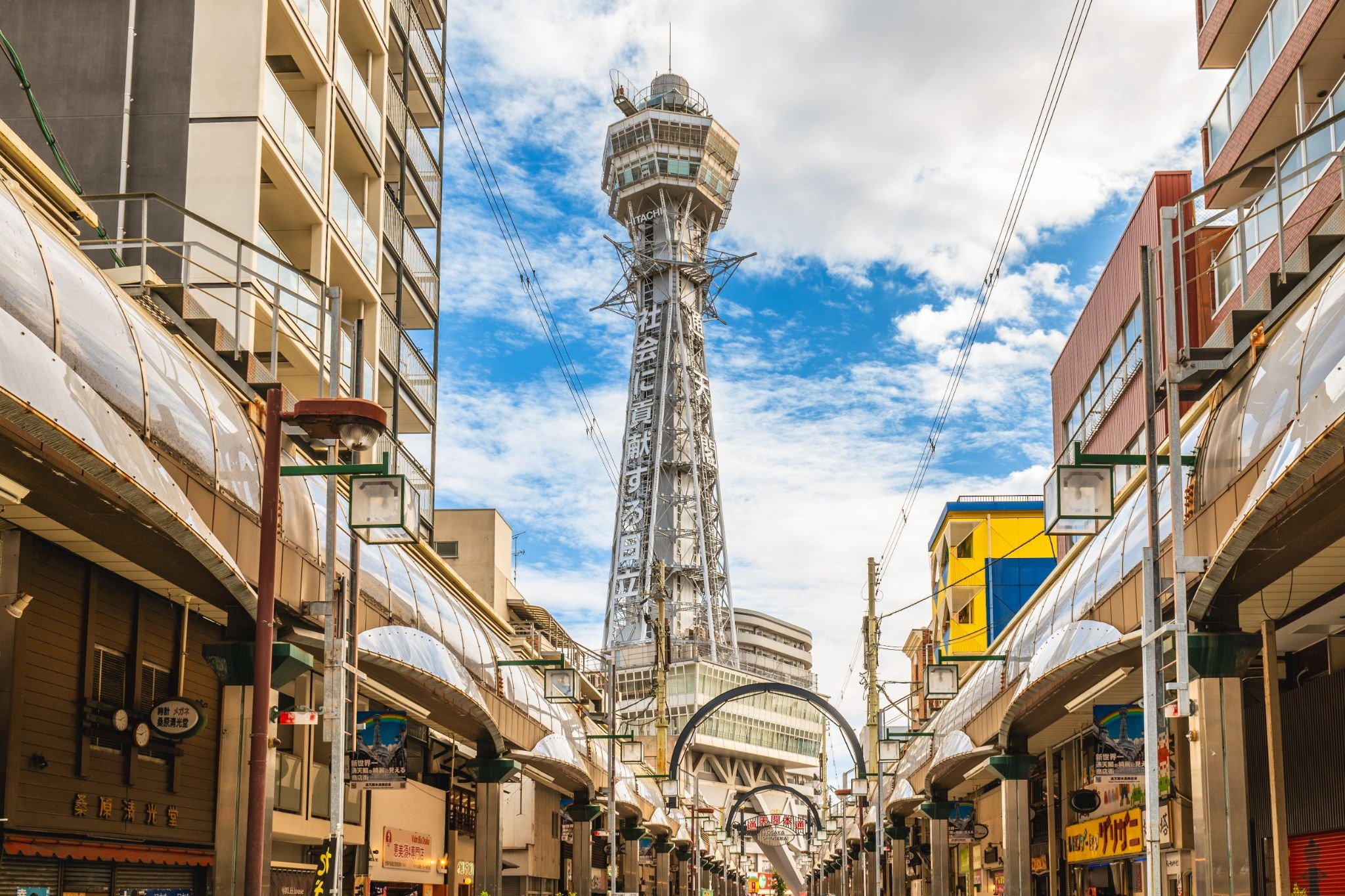 Tsutenkaku Tower rising above the streets of Shinsekai in Osaka under a bright blue sky.
