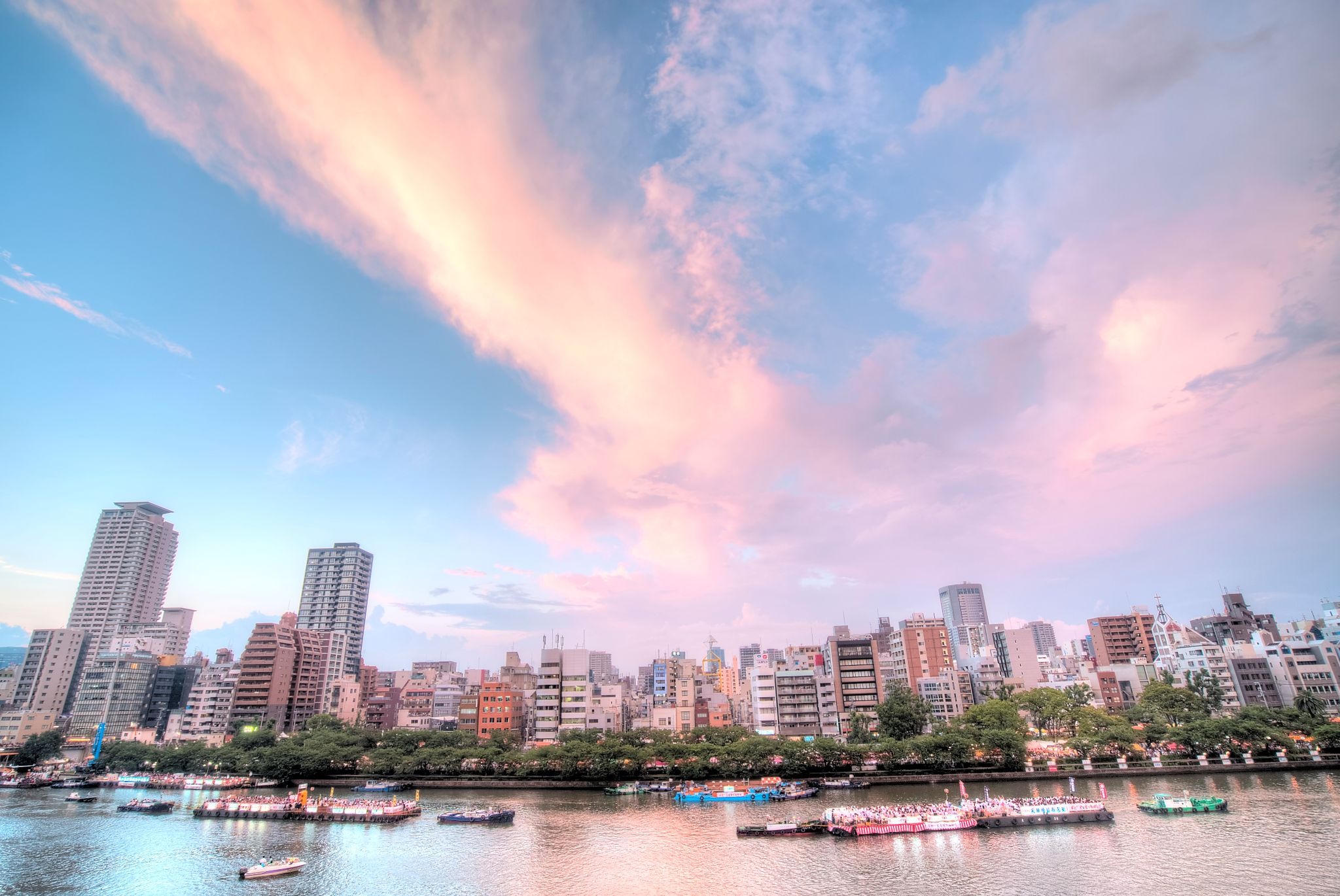 Tenjin Matsuri boat procession on the Okawa River in Osaka at sunset, with festival boats and the city skyline.