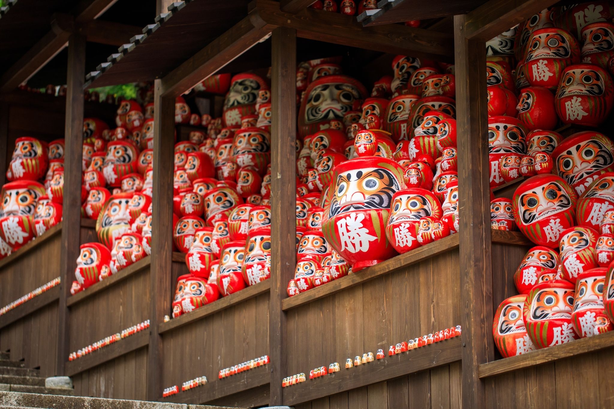 Katsuoji Temple in Minoh, Osaka, surrounded by red daruma dolls and forested mountain scenery.